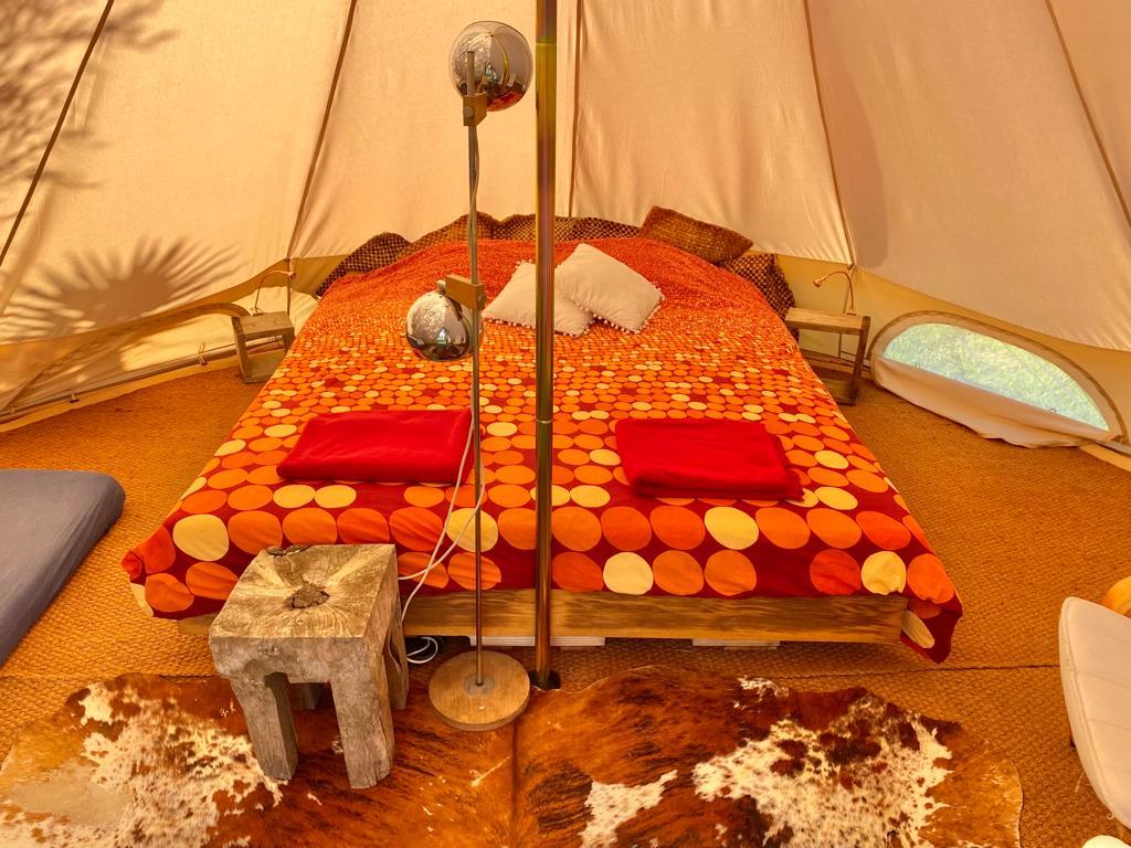 Bedroom with made bed colored in oranges and reds inside the lotus glamping tent