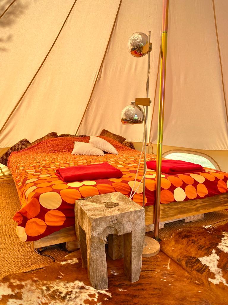 Made beds with oranges and reds inside the lotus glamping tent