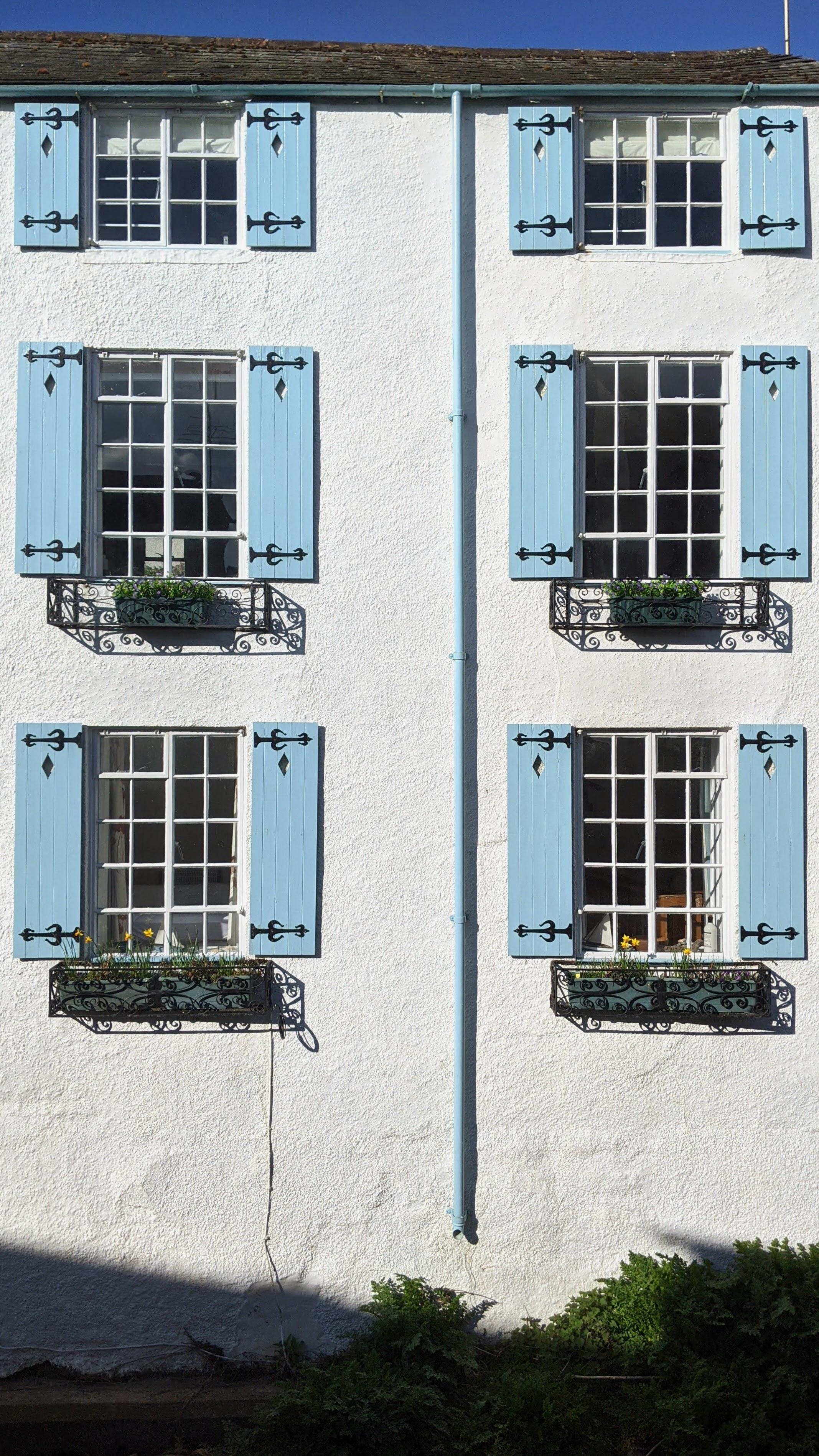 The french style blue wooden shutters of this exterior period holiday cottage property where the river Lym flows underneath it and alongside, the best views of the river with sounds of running water to fall asleep to 