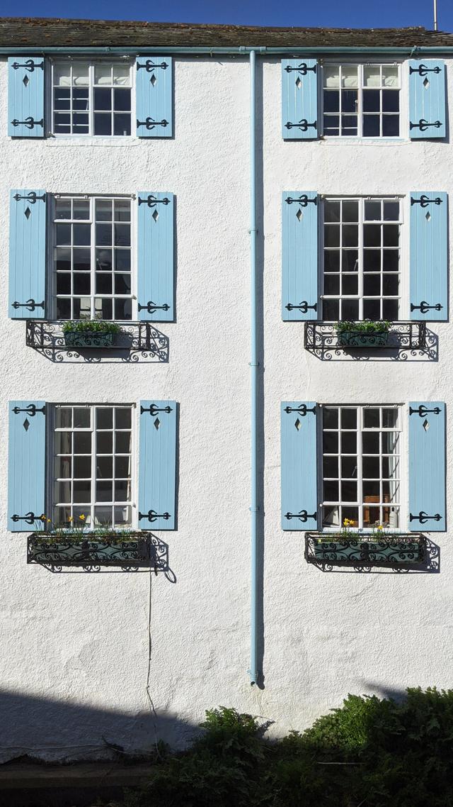 The french style blue wooden shutters of this exterior period holiday cottage property where the river Lym flows underneath it and alongside, the best views of the river with sounds of running water to fall asleep to 