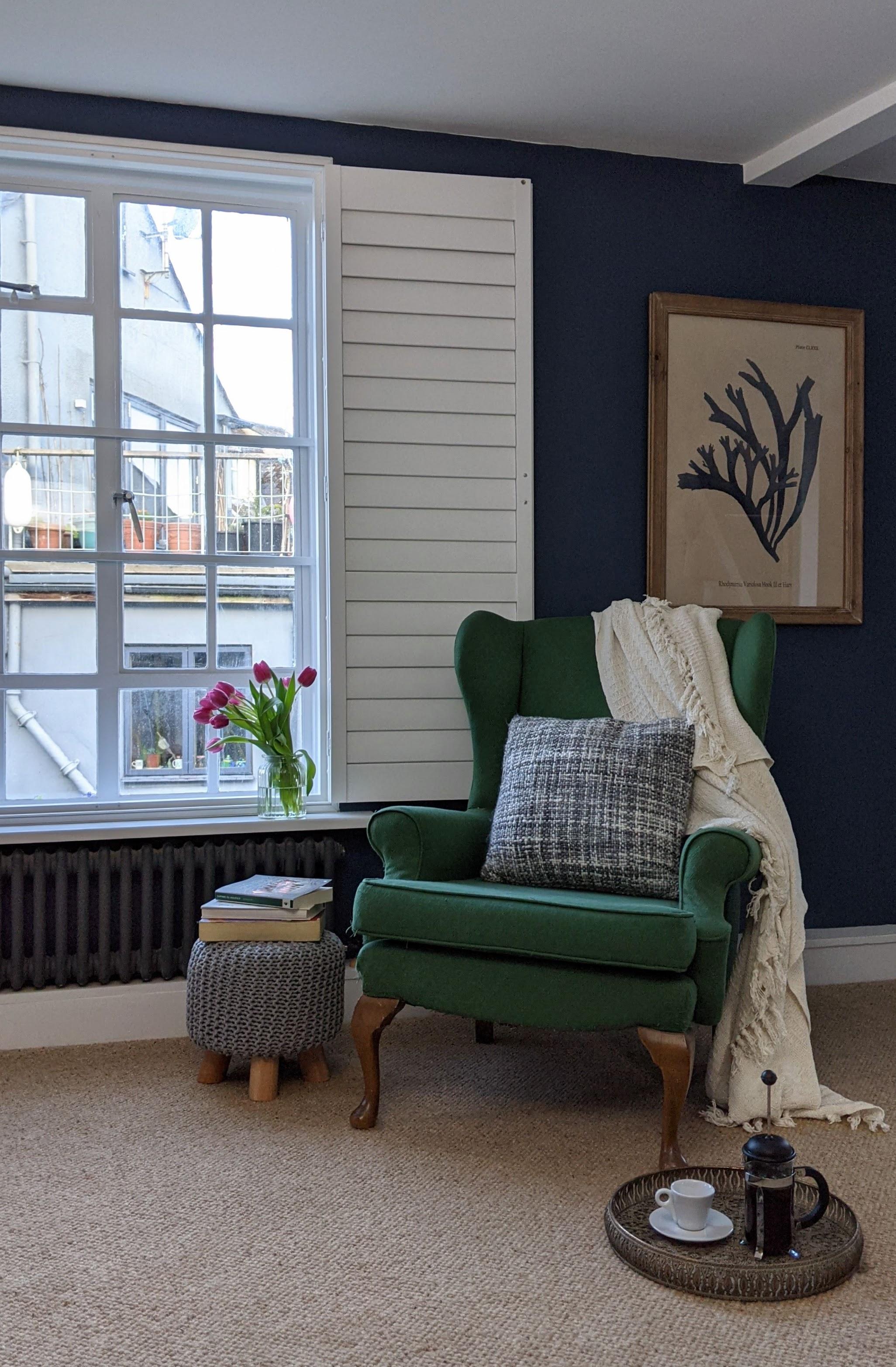 Relax in this easy chair an antique chair paired with contemporary fabrics and art next to the window with white interior shutters and blue exterior shutters it's the most relaxing stay with views up the River Lym 