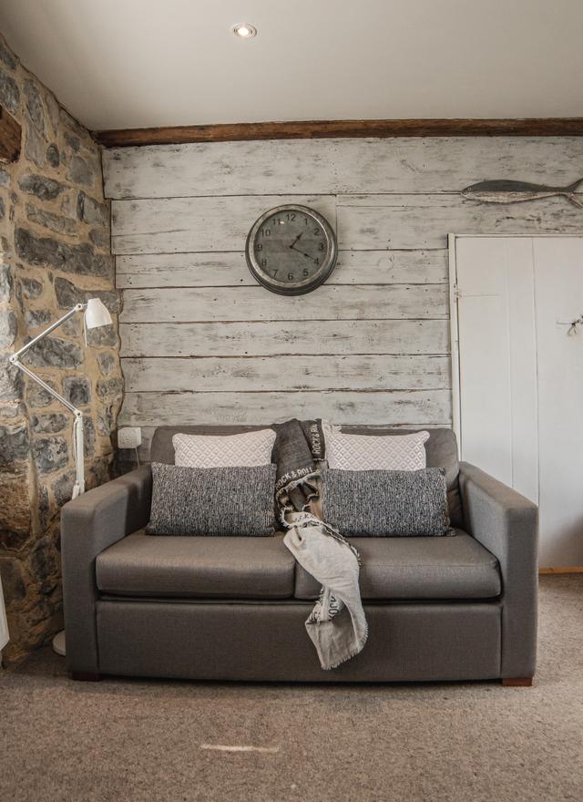 Wooden clad walls and stone work with comfy sofa and footsool in The Majors lounge with feature clock and soft blankets for a cosy winter weekend getaway to central Lyme Regis