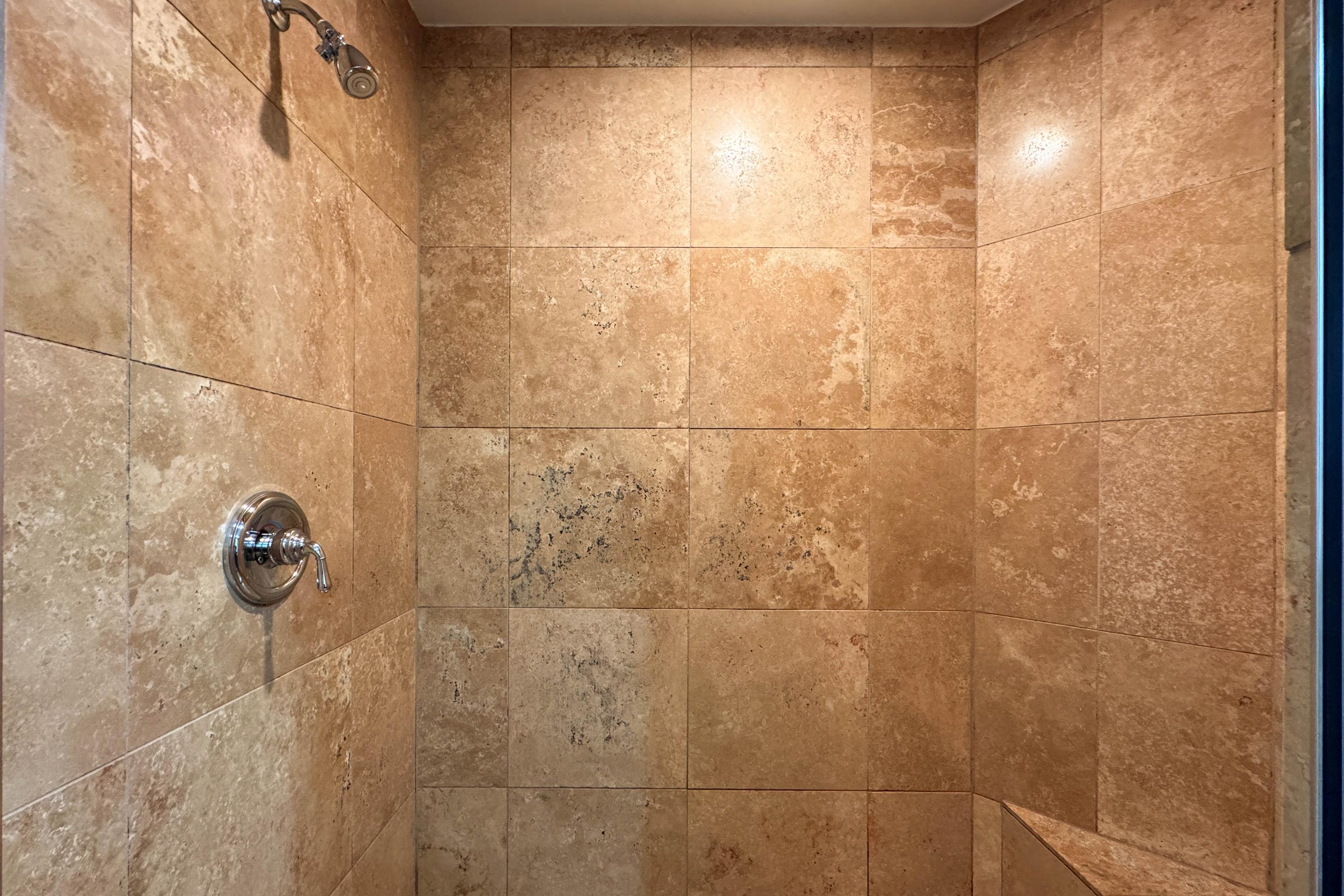 Large, luxurious Travertine walk-in shower with seating bench.