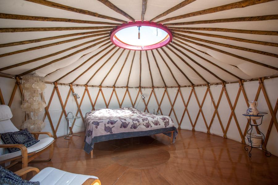 Inside of the natural lit mongolian tent with queen-sized bed and chairs