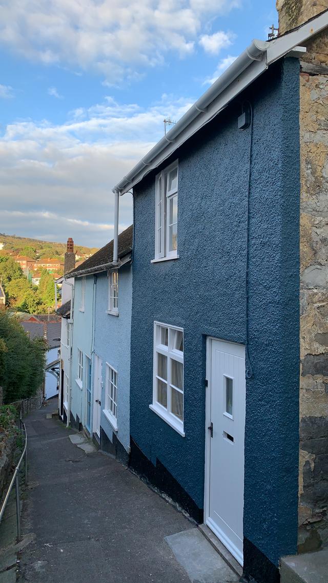 Seahorse Cottage front entrance from Sherborne Lane painted blue with two hundred year old stone walls next to other stylish painted colourful cottages in central Lyme Regis