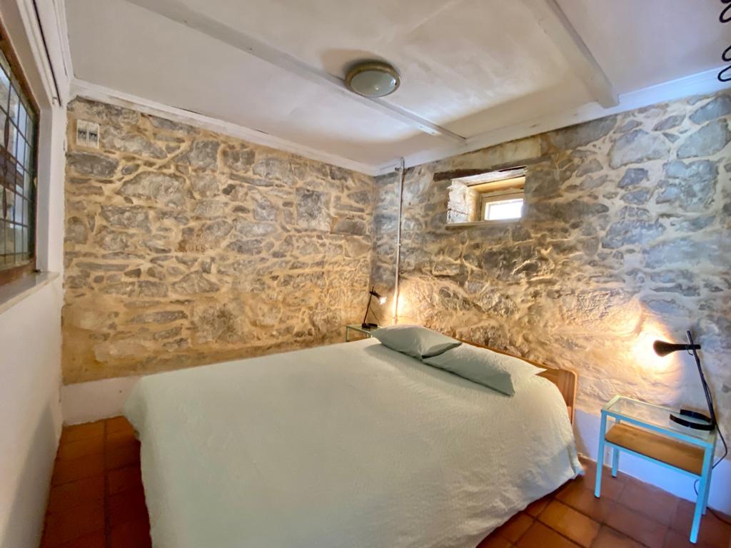 master bedroom with rustic walls, a made bed, and clay colored floor tiling 